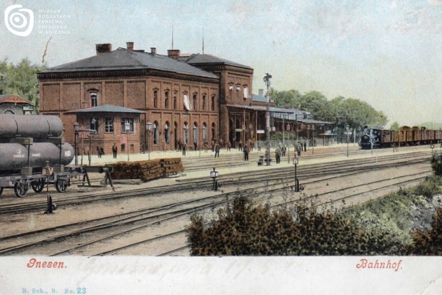 Widok głównego budynku dworca kolejowego w Gnieźnie od strony południowo-zachodniej. Dworzec gnieźnieński otwarto uroczyście w 1872 r. Pierwsze połączenie kolejowe uzyskał ze stacjami w Poznaniu i Inowrocławiu. W latach 1964-1966 został częściowo rozebrany i całkowicie przebudowany, tracąc bezpowrotnie swój zabytkowy charakter. Na drugim planie widoczny peron drugi dworca, z wznoszącym się na nim wówczas semaforem i dochodzącą do peronu z lewej strony bocznicą (ślepym torem). Pocztówka fotograficzna, kolorowana, z około 1890-1896 r., wydana przez Paula Raucha w Gnieźnie.
