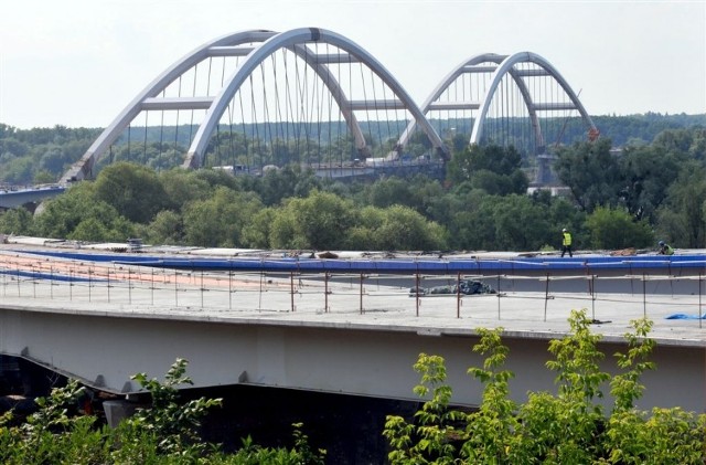 Budowa nowego mostu w Toruniu w lipcu 2013 r. Najbardziej widowiskowe prace są obecnie prowadzone pod łukami mostowymi, gdzie wykonawca podwiesza i montuje płyty pomostu. Elementy powstają w wytwórni w Płocku i drogą wodną są transportowane na plac budowy.