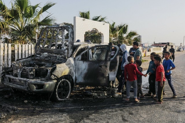 Ludzie stoją obok zniszczonego samochodu organizacji pozarządowej World Central Kitchen (WCK) wzdłuż drogi Al Rashid, pomiędzy Deir Al Balah a Khan Younis na południu Strefy Gazy, 2 kwietnia 2024.