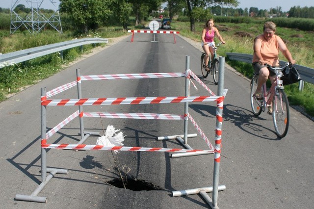 Przez niewielką dziurę w asfalcie widać kilkudziesięciocentymetrową szczelinę na prawie całej szerokości drogi.