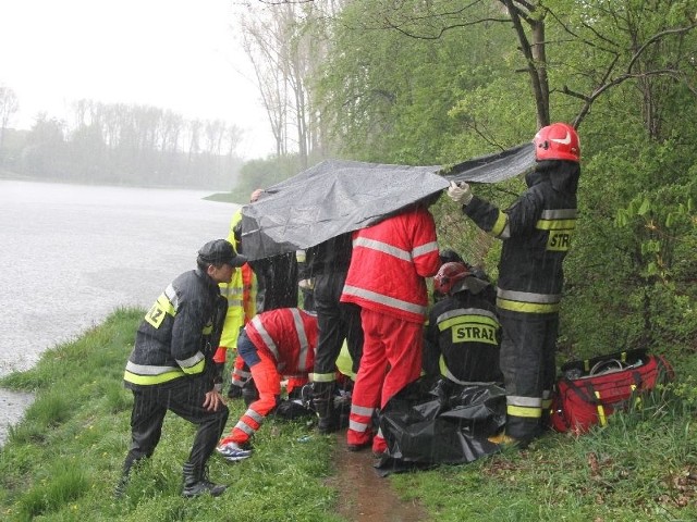 Ratownicy z ambulansu prowadzili reanimację mężczyzny osłaniani przez strażaków przed ulewnym deszczem.