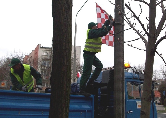 Pracownicy służby drogowej rozwieszają flagi Polski i Głogowa wzdłuż głównych ulic w mieście.
