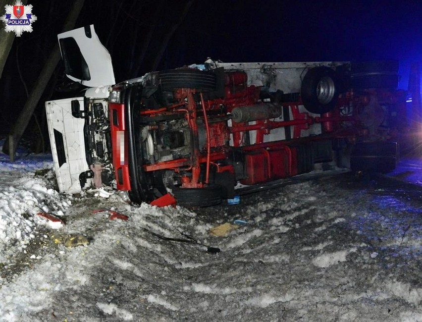 Leżąca na poboczu, na boku ciężarówka z uszkodzoną kabiną...