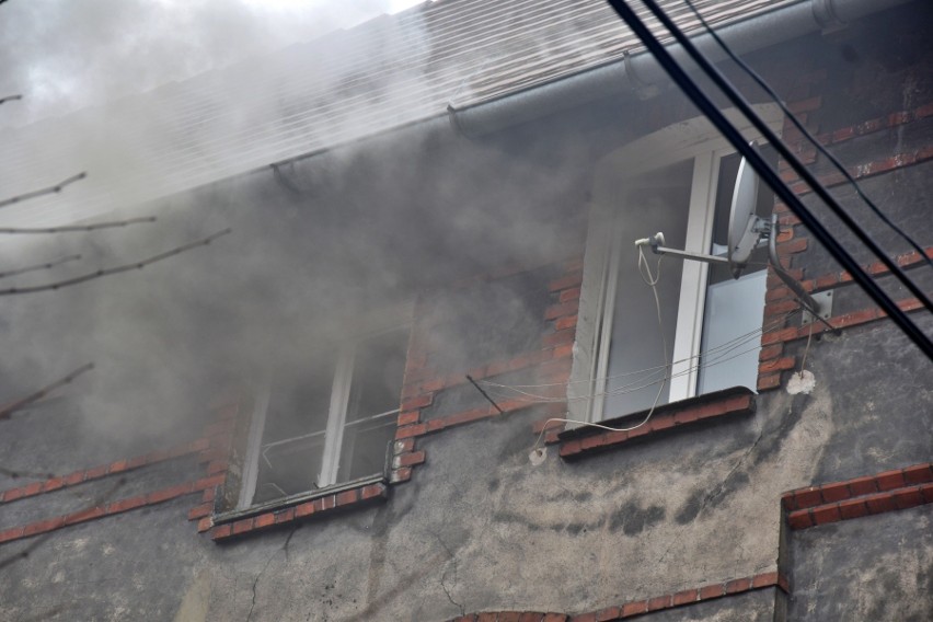 Z okien wydobywają się kłęby dymu. Na miejscu są strażacy