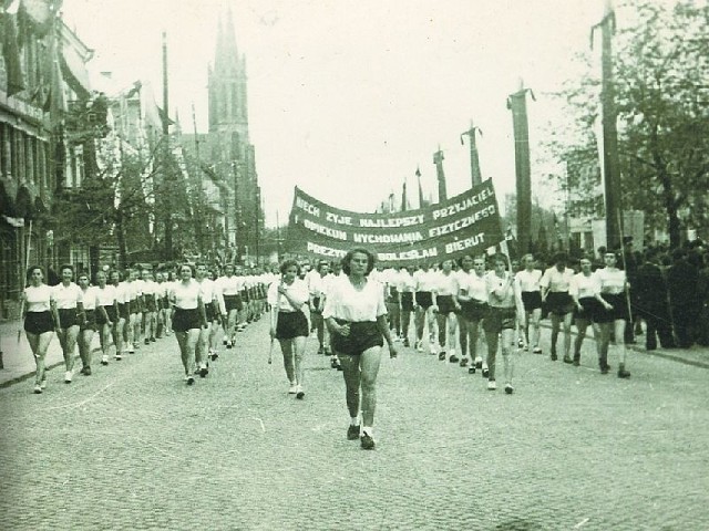 Kolumna sportowa z Liceum Ogólnokształcącego Żeńskiego nr 2 w pochodzie 1-majowym w 1951 r.  Idziemy ulicą Warszawską. W głębi kościół św. Wojciecha.