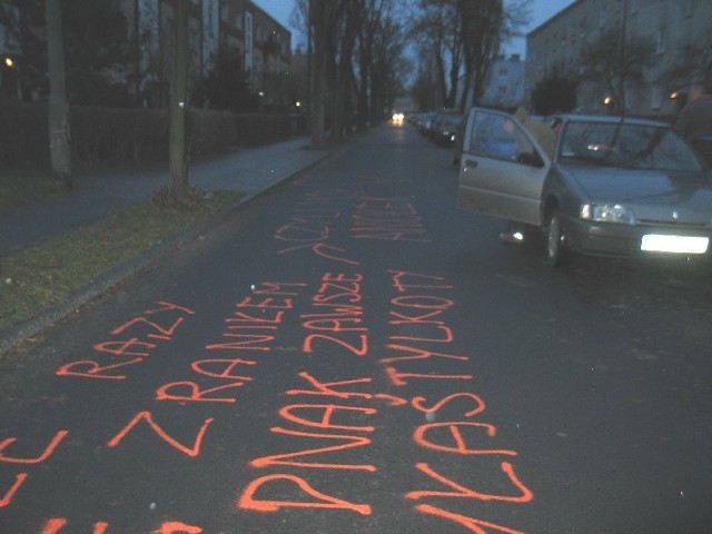 Pomarańczowe napisy na jezdni są trwałe i nie zmyje ich jeden deszczyk. Wygląda, że ktoś używał pomarańczowej kredy lub farby w sprayu.