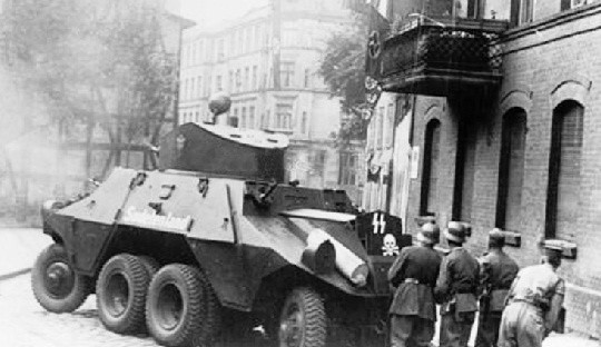 Opancerzony  wóz  bojowy "Sudetenland&#8221;­­ atakuje budynek urzędu pocztowego, obok obserwujący policjanci. 