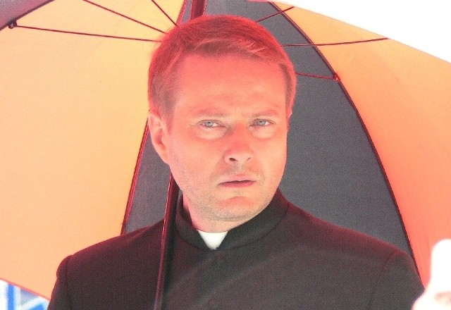 Ojciec Mateusz, w tej roli Artur Żmijewski cgronił się przed słońcem pod wielkim parasolem.