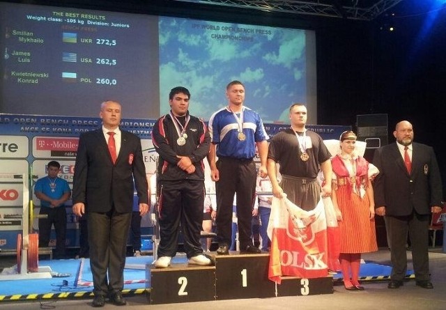 Konrad Kwietniewski (z flagą narodową) w Pilznie w Czechach wywalczył brązowy medal mistrzostw świata juniorów w wyciskaniu sztangi na ławeczce