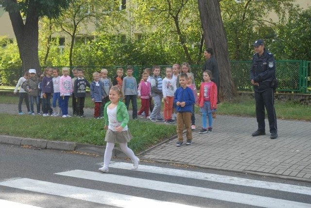 Dzieci wraz z nauczycielką Alicją Karpowicz i policjantem przed szkołą ćwiczyły prawidłowe przechodzenie przez jezdnię.