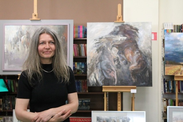 Samantha Glińska na tle swoich obrazów w  bibliotece na wernisażu. Jej prace można oglądać do końca czerwca.