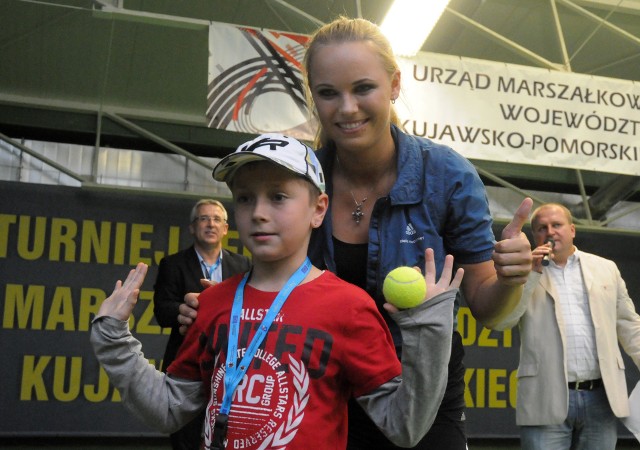 W niedzielę wygrała turniej WTA Finals w Singapurze z udziałem najlepszych ośmiu tenisistek sezonu (nieoficjalne mistrza świata), pokonując w finale Amerykankę Venus Willimas 6:4, 6:4. Przy okazji zarobiła 2,2 mln dolarów i awansowała z 6. na 3. pozycję w rankingu WTA. Ale kiedyś jako nr 1 odwiedziła Bydgoszcz. Pamiętacie?18 września 2011 roku Karolina Woźniacka, Dunka polskiego pochodzenia (ojciec Piotr, były piłkarz, mama Anna była reprezentacyjna siatkarka) przyleciała do Polski prosto z Nowego Jorku. US Open nie wygrała, bo w półfinale zatrzymała ją Serena Williams. Ale w tym momencie 21-latka od 48 tygodni liderowała światowemu rankingowi WTA.Do Bydgoszczy przybyła razem z ojcem na zaproszenie marszałka województwa kujawsko-pomorskiego Piotra Całbeckiego, poprowadziła trening i wręczyła nagrody w turnieju dla dziewcząt i chłopców w kategoriach wiekowych do lat 10 i 12 w SKT „Centrum” przy ul. Nowotoruńskiej.Woźniacka, przyjaciółka Agnieszki Radwańskiej, która w lipcu gościła Karolinę na swoim ślubie, 6 lat temu odwiedziła też Toruń. A do Bydgoszczy wróciła później, gdy kręciła teledysk do singla „Oxygen”. Na planie zdjęciowym pojawili się również Kuba Wesołowski oraz pies Rocky, znani z serialu „Komisarz Alex”. [sc]POLUB NASZ PROFIL NA FACEBOOKU[/sc]