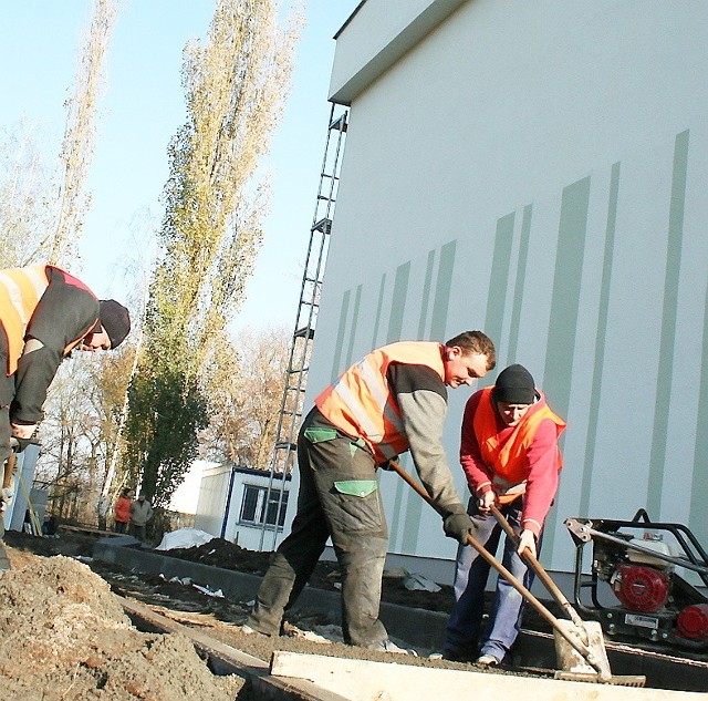 Pracownicy spółki "Budrox" wytyczają ścieżkę wokół murów nowej sali gimnastycznej