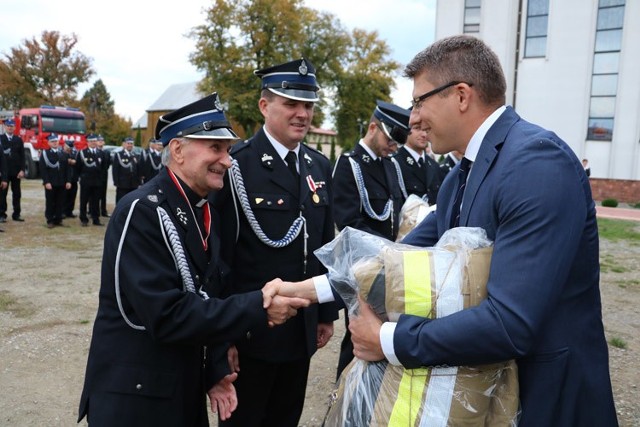 Wiceminister sprawiedliwości Marcin Warchoł przekazuje strażakom specjalne ubrania, z lewej ksiądz Józef Turoń