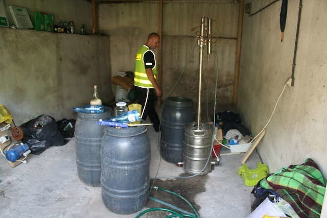 Policjanci wśród odkrytej w jednym z garaży aparatury do produkcji bimbru 