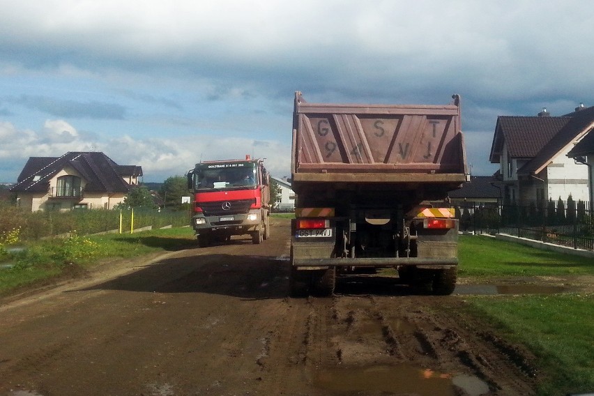 Ciężkie ciężarówki rozjeżdżają drogę obok domków...