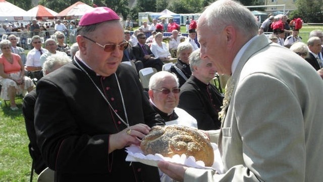 Wój Lech Skarbiński dzieli się dożynkowym chelem z księdzem biskupem Bogdanem Wojtusiem.