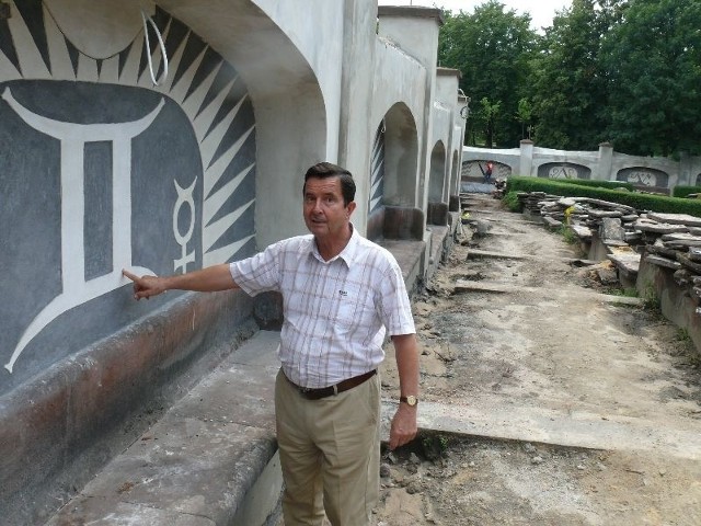 Piotr Maciej Przypkowski, dyrektor muzeum prezentuje mur, w którego wnękach są dekoracje przedstawiające znaki zodiaku, znaki żywiołów i znaki planet.