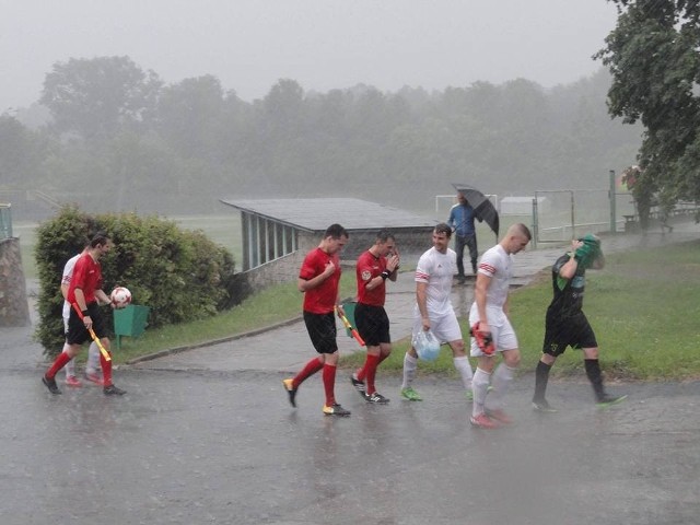 Zawodnicy i sędziowie schodzą z boiska, mecz został przerwany przez ulewę.