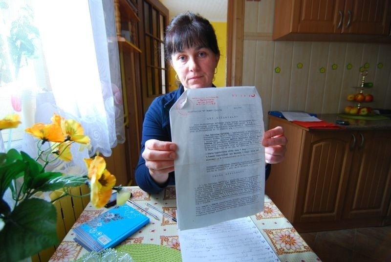 Edyta Łagodzińska pokazuje akt własności na połowę domu....