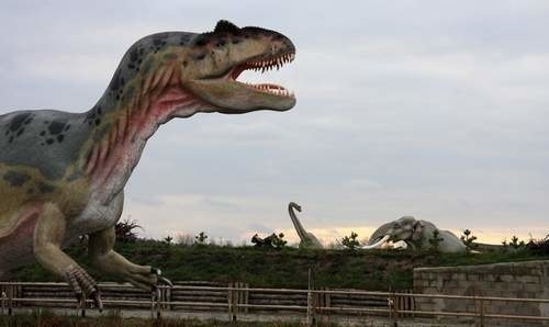 Na pierwszym planie po lewej allozaurus, w oddali słoń leśny, a w tle brachiozaur.