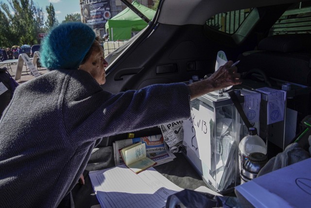 Starsza kobieta oddająca swoją kartę do głosowania do skrzynki ustawionej w bagażniku samochodu podczas głosowania w referendum w sprawie przyłączenia kontrolowanych przez Rosję regionów Ukrainy do Rosji, Mariupol 25 września 2022