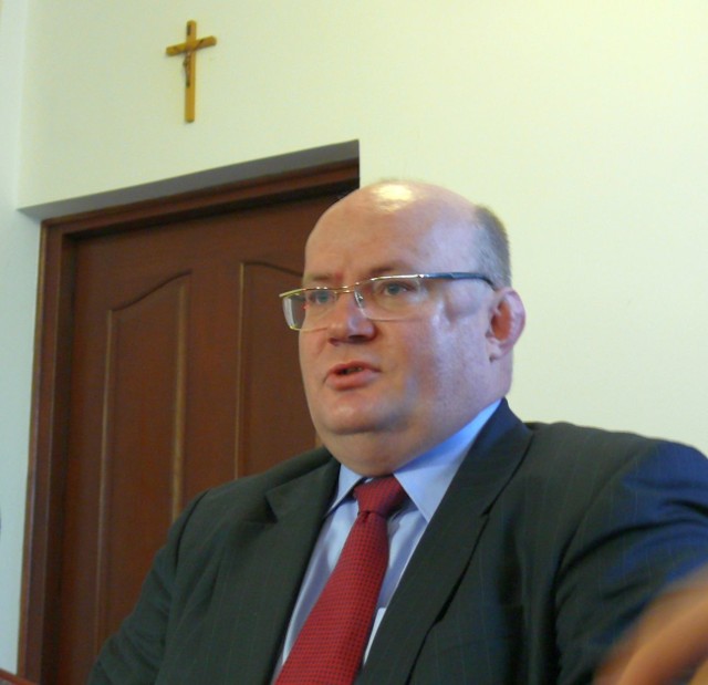 Prezydent Andrzej Szlęzak na konferencji prasowej przy drzwiach do swojego gabinetu, nad którymi wisi krzyż.