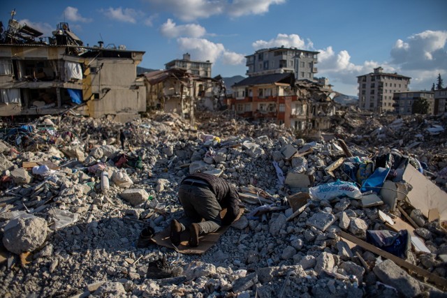 Mężczyzna modlący się na gruzach zawalonego w wyniku trzęsienia ziemi budynku w Turcji