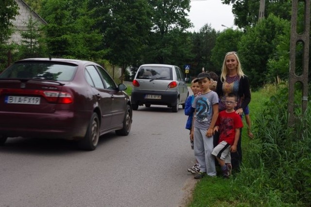 Dzieci z Niewodnicy Kościelnej oraz ich rodzice pokonują ruchliwą i niebezpieczną drogę. Nie ma tu nawet chodnika, więc idą poboczem. Mijają ich jadące szybko samochody.