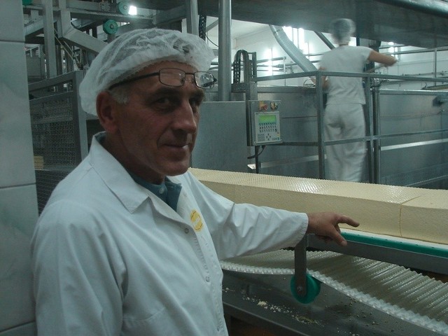 Kierownik zmiany Grzegorz Olkiewicz wskazuje na taśmę z surowym serem, który za chwilę zostanie pokrojony na części.