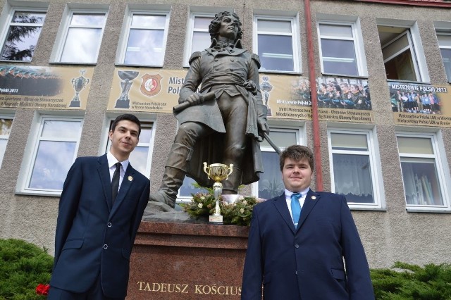 Bartek Kowalik i Michał Puzio z pucharem przy pomniku patrona szkoły budowlanej.