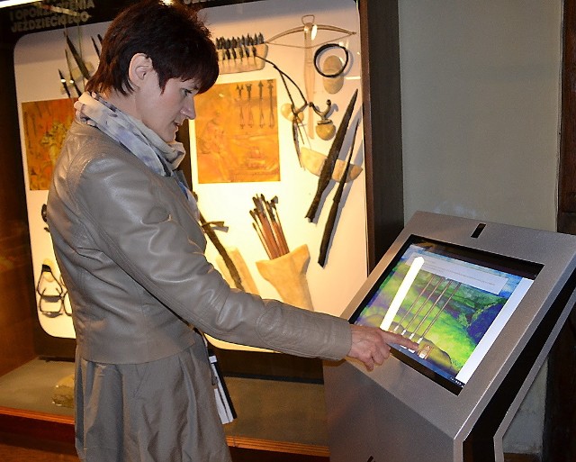 Małgorzata Kurzyńska, dyrektor muzeum, zachęca zwiedzających do zapoznania się w eksponatami. Przy okazji można przśledzić na monitorze, jak niegdyś  budowano wieżę z drewnianych pali.