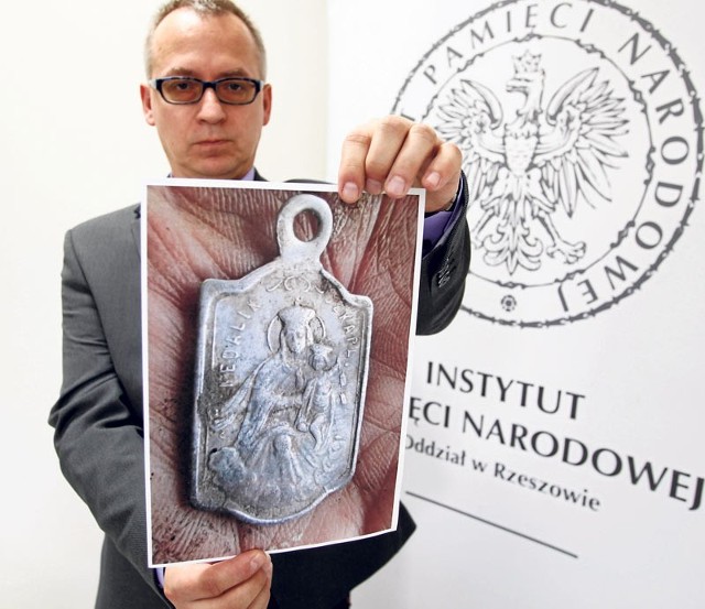 Prokurator Grzegorz Malisewicz prezentuje zdjęcie jednego ze znalezionych przy ludzkich szczątkach szkaplerzy z wizerunkiem Matki Bożej z Dzieciątkiem.