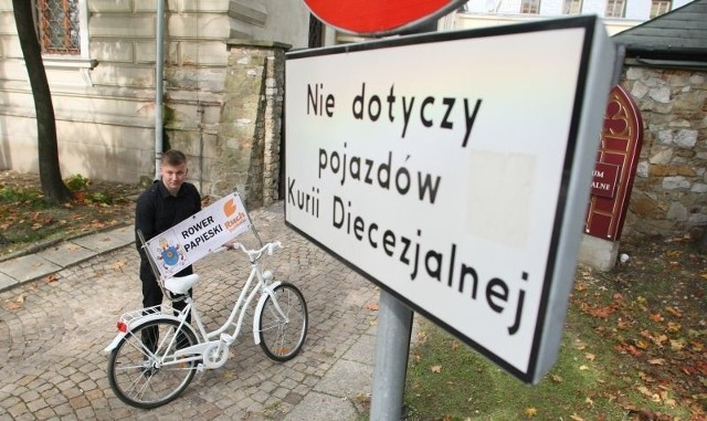 Adrian Bieluń, szef Ruchu Młodych w Świętokrzyskiem, prezentuje biały rower dla biskupa Ryczana.