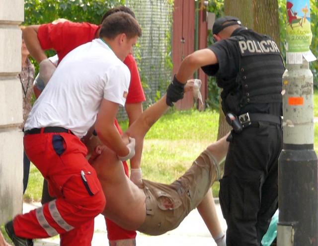 Policjanci pomagają ratownikom przenieść rannego mężczyznę na nosze.