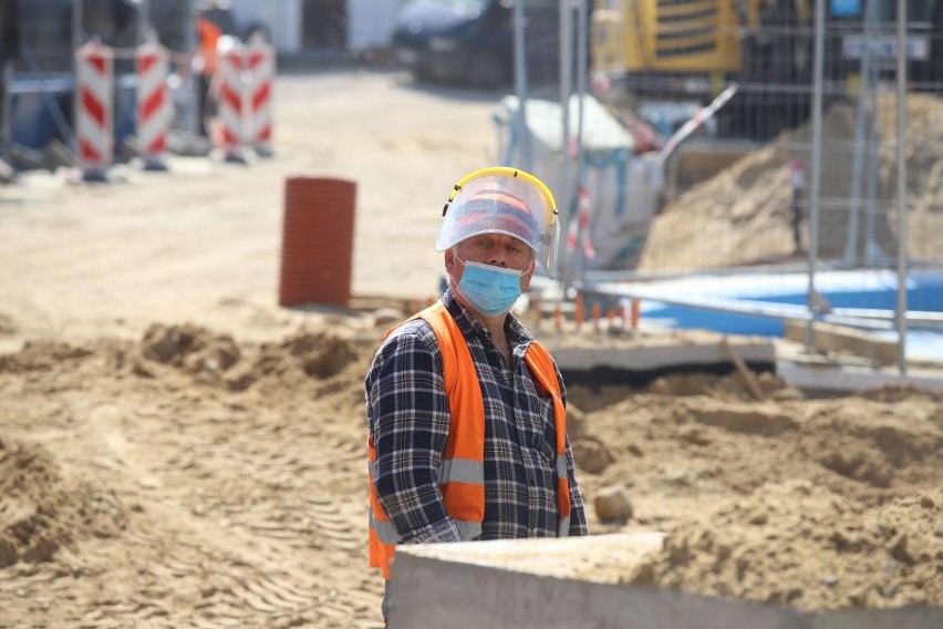 Robotnicy na placu budowy pracują w ochronnych rękawicach,...