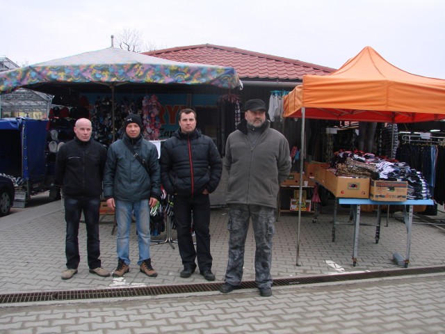 Kupcy  na placu targowym w Oświęcimiu  przed dwoma stanowiskami: pomarańczowy daszek traktowany jest jako namiot i trzeba za niego dodatkowo zapłacić, kolorowy parasol można ustawić bez opłaty