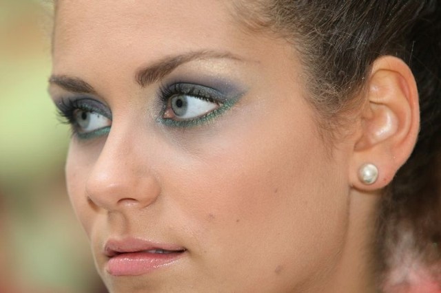 Rozświetlony zielono-fioletowy makijaż oczu tworzy całość z nakryciem głowy.