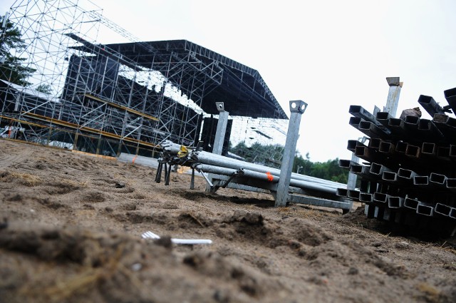 Do rozpoczęcia Przystanku Woodstock 2017 zostało dziewięć dni. Tymczasem na festiwalowej łące w Kostrzynie w dalszym ciągu trwa wielka budowa. Duża Scena "uzbrajana" jest w oświetlenie, trwa obijanie jej konstrukcji deskami, stoi też konstrukcja Małej Sceny. Co jeszcze dzieje się na woodstockowej łące w Kostrzynie nad Odrą?Pogoda nie rozpieszcza ekip, uwijających się przy budowie woodstockowej infrastruktury. Od dwóch dni pada deszcz, jest chłodno, mokro, a festiwalowa łąka pod kołami ciężkiego sprzętu w wielu miejscach zmienia się w grzęzawisko. Mimo tych niedogodności prace idą pełną parą. Gotowe są już namioty na pasażu handlowym i namioty, z których będziecie mogli kupić jedzenie. Gotowa jest też Pokojowa Wioska Kryszny, zamontowane są krany i natryski. Na festiwalową łąkę wciąż przyjeżdżają ciężarówki po brzegi wyładowane elementami woodstockowej infrastruktury.W momencie, gdy byliśmy na polu, trwał akurat rozładunek tira, który przywiózł na woodstockowe pole barierki. Będzie nimi ogrodzony teren przed Dużą Sceną. To właśnie te barierki będą wyznaczały teren imprezy masowej, na którym obowiązywał będzie zakaz spożywania alkoholu.Wszystkie informacje o Przystanku Woodstock 2017 w Kostrzynie nad Odrą:  Przystanek Woodstock 2017: koncerty, zdjęcia, filmy, informacjeBardzo dużo dzieje się przy Dużej Scenie. Ekipa Pokojowego Patrolu (tzw. kwaterka) obija front sceny deskami. Już drugi tydzień 12 osób z kwaterki jest w Kostrzynie i pracuje przy budowie woodstockowego miasta. Na scenie specjalistyczna firma zajmuje się montażem oświetlenia, które nada Dużej Scenie specyficzny i niepowtarzalny klimat. Przypomnijmy, projekt oświetlenia sceny co roku jest inny. Na polu jest już konstrukcja Małej Sceny, stoi namiot, w którym znajdzie się woodstockowy market, trwa budowa wioski piwnej oraz płatnego pola namiotowego Toi-Camp.Przystanek Woodstock 2017 rozpoczyna się w czwartek, 3 sierpnia i potrwa do soboty, 5 sierpnia. Będzie to 23. edycja imprezy i 14. z z rzędu, organizowana w Kostrzynie nad Odrą.Chcesz wiedzieć kto zagra na Przystanku Woodstock 2017? Przystanek Woodstock 2016: zespoły, koncerty kto zagra