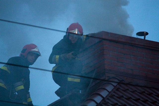 Strażacy gaszą płonącą w kominie sadzę.