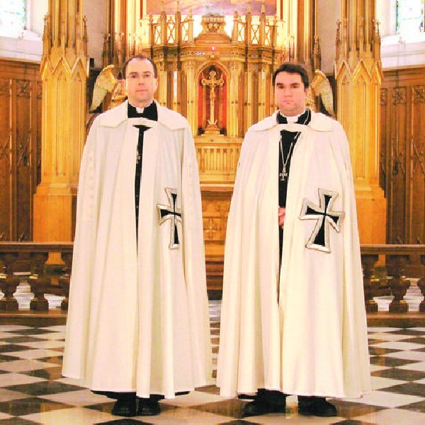 Ks. Waldemar Woźniak (z lewej) w białym płaszczu z czarnym krzyżem, w towarzystwie brata z zakonu krzyżackiego