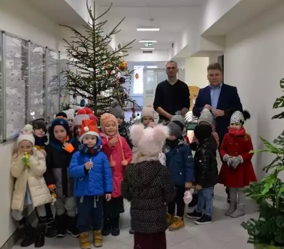 To już kolejny rok, kiedy przedszkolaki ubierały choinkę w Urzędzie Miasta i Gminy Połaniec. Towarzyszył im burmistrz Jacek Tarnowski, jego zastępca Roman Adamczak oraz inni pracownicy placówki. Ubieranie choinki przez przedszkolaki to w połanieckim urzędzie miasta już tradycja. W tym roku najmłodsi ponownie z wielkim zapałem, pilnością i zaangażowaniem przystąpili do tego zadania. Kiedy na drzewku zawisły już zawieszki, bombki i łańcuchy, mali goście zaprezentowali krótki program artystyczny, tym samym składając serdeczne życzenia burmistrzowi oraz wszystkim pracownikom urzędu. W podziękowaniu za trud włożony w przystrajanie choinki oraz za wyjątkowe odśpiewanie kolęd, przedszkolaki zostały obdarowane słodyczami oraz pluszowymi maskotkami.  Zobacz więcej na kolejnych slajdach>>>