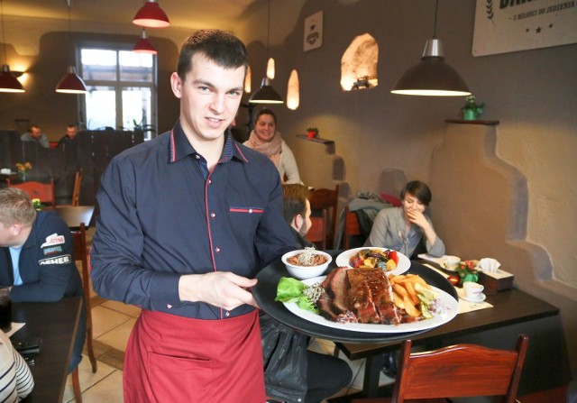 Kelner, pana Adam, prezentuje danie Barbecue Dinne Plate. To m.in. mostek wołowy, żeberka wieprzowe i kiełbaski wieprzowo-wołowe. Cena – 30 zł.