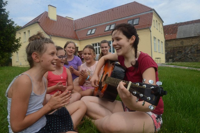 Anna Skurzyńska (gra na gitarze) z koleżankami na tle świetlicy.