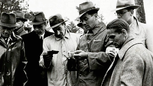 Józef Mackiewicz (po środku, w jasnym płaszczu) przegląda gazety i dokumenty wydobyte z kieszeni zamordowanych na miejscu ekshumacji w Katyniu