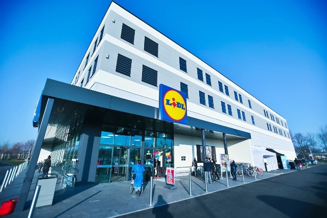 Kolejny Lidl we Wrocławiu już otwarty. Od czwartkowego poranka można już robić zakupy w sklepie położonym przy ulicy Buforowej, na granicy trzech dużych osiedli: Jagodna, Brochowa i Wojszyc. Budynek z daleka zwraca uwagę z powodu nietypowej dla tej sieci wysokości, obiekt ma aż kilkanaście metrów. Taki projekt był spowodowany wymogami planu zagospodarowania przestrzennego. Zgodnie z jego zapisami, budowane tam obiekty muszą mieć więcej niż 15 metrów i nie więcej niż 23 metry wysokości. Dlatego też Lidl sprawia wrażenie dwupiętrowego. W rzeczywistości jednak sala sprzedaży zajmuje tylko parter. Od czwartkowego poranka zrobiło się tam bardzo tłoczno, a chętnych na zakupy w atrakcyjnych cenach zdecydowanie nie brakuje. Co można kupić w dniu otwarcia? W promocji są m.in. kuchenki mikrofalowe, telewizory czy roboty kuchenne. Zobacz zdjęcia i ceny na kolejnych slajdach w galerii. Przejdź dalej przy pomocy strzałek lub gestów na ekranie smartfona.