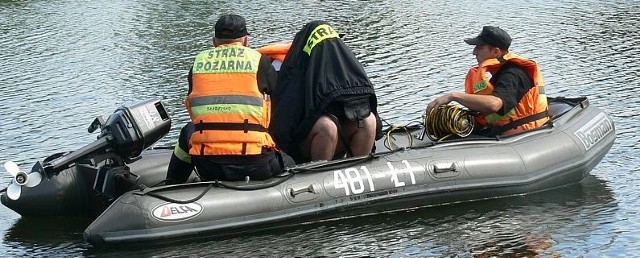 Strażacy z pontonu przeszukiwali wyrobisko w poszukiwaniu zaginionego 23-latka. Widoczny na zdjęciu strażak z głową zakrytą kurtką obserwuje dno zbiornika za pomocą kamery podwodnej.
