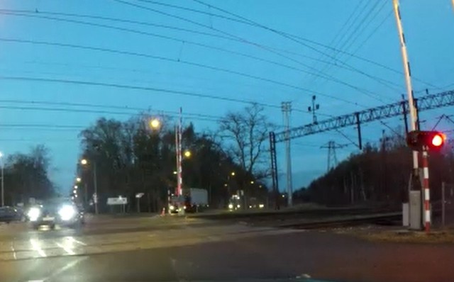 Kierowca porsche wyprzedza na skrzyżowaniu i przejeżdża przez przejazd kolejowy, gdy jeszcze palą się czerwone światła ostrzegawcze.