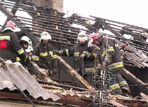 Strażacy dogaszają ogień tlący się na dachu  domu.