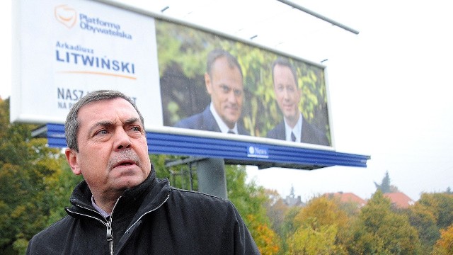 Bartłomiej Sochański na tle plakatu wyborczego Arkadiusz Litwińskiego w towarzystwie Donalda Tuska.